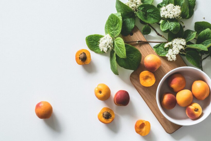 A bright still life of fresh apricots and blossoms on a cutting board, perfect for healthy eating.