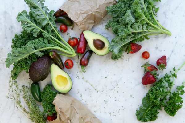 Top view of fresh avocados, kale, tomatoes, and peppers arranged on a marble surface.