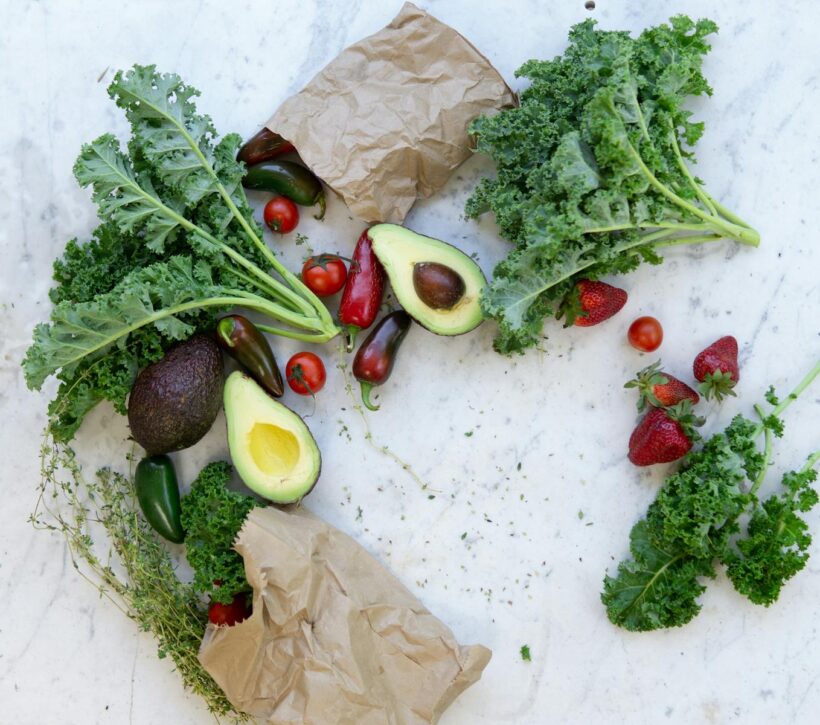 Top view of fresh avocados, kale, tomatoes, and peppers arranged on a marble surface.